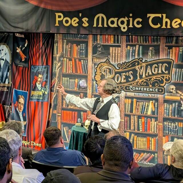 A magician presenting on the Poe's Magic Conference stage before a live audience